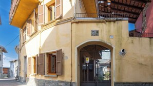 A yellow building with a stone base, a metal gate, and a small balcony. - Cosy apartment for 4 people with WIFI and balcony (Brovello)