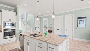 A kitchen with white cabinets, stainless steel appliances, granite countertops, pendant lighting, and a view of the living area. - 🌊🏖️ Sea Haven | Sound Views, Firepit + Community Pool | Navarre Beach (Navarre Beach)