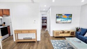 Ein modernes Wohnzimmer mit einem Holztisch, einem blauen Sofa und einem Fernseher, der eine Strandansicht zeigt.
