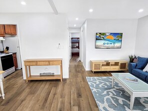 Ein modernes Wohnzimmer mit einem Holztisch, einem blauen Sofa und einem Fernseher, der eine Strandansicht zeigt.