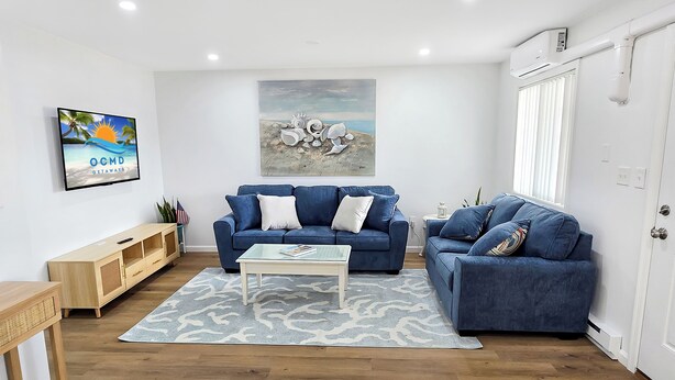 Ein Wohnzimmer mit zwei blauen Sofas, einem Couchtisch, einem Fernseher und Kunstwerken an der Wand.