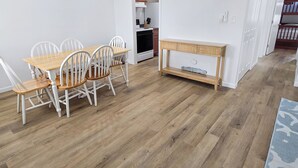 Ein Essbereich mit einem Holztisch und weißen Stühlen, einem Holzkonsole und einer Küche im Hintergrund.