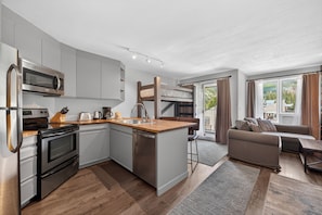 A modern kitchen with a built-in microwave, oven, and dishwasher, a wooden counter, and a dining area with a sofa and table. - Renovated studio, private deck, mt views, easy access to WP Resort (Winter Park)