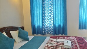 A bedroom with a bed, pillows, a blanket, a floral bedspread, curtains, and a wall-mounted light fixture. - REJOICE HOMESTAY  (Darjeeling)