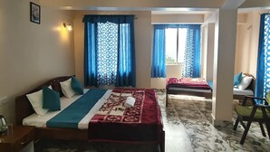 A room with a bed, a chair, a table, and a window with curtains. - REJOICE HOMESTAY  (Darjeeling)