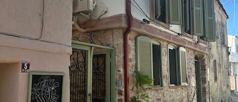 Un edificio con un letrero que dice 'Chori Avlu', fachada de piedra, calle adoquinada y una reja metálica.