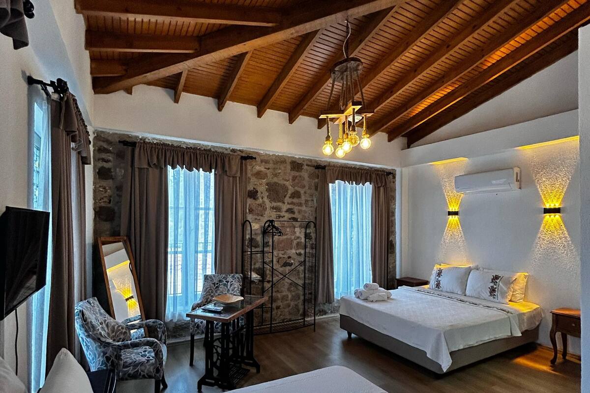 Una habitación con techo de madera, dos camas, una pared de piedra, una mesa y una silla.