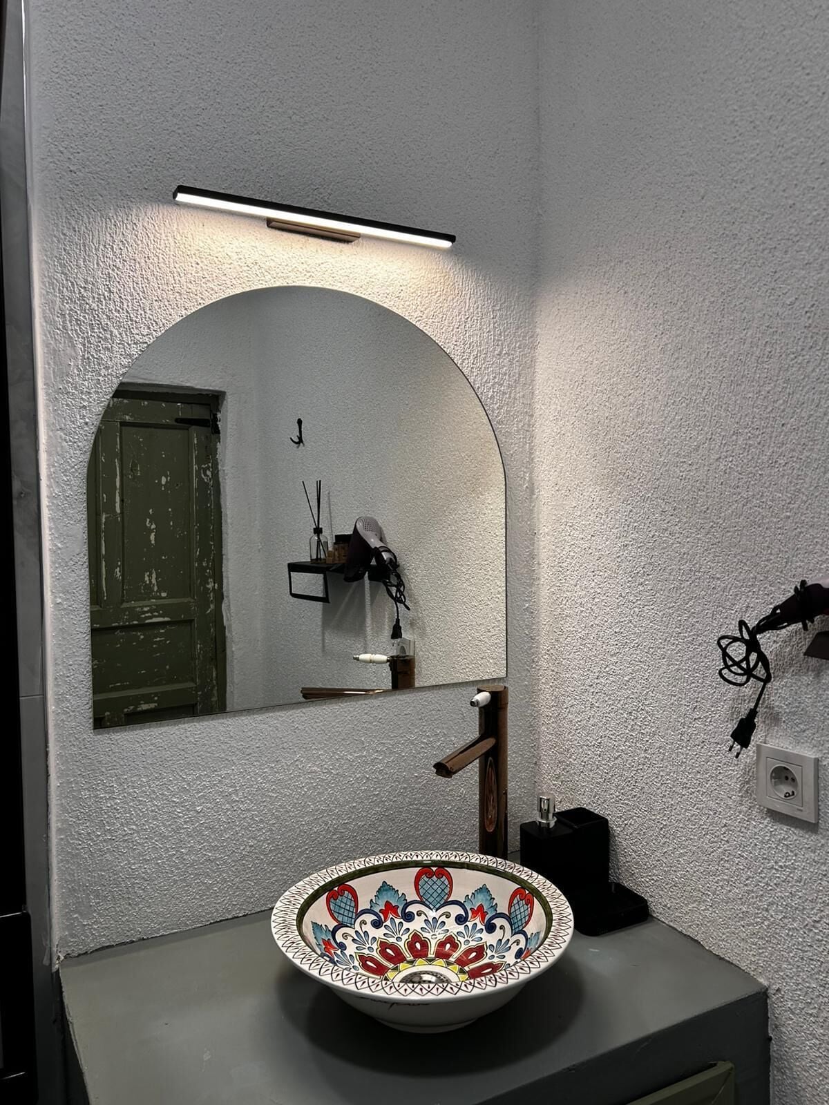 A bathroom with a white sink, a mirror with an arched top, and a green door.