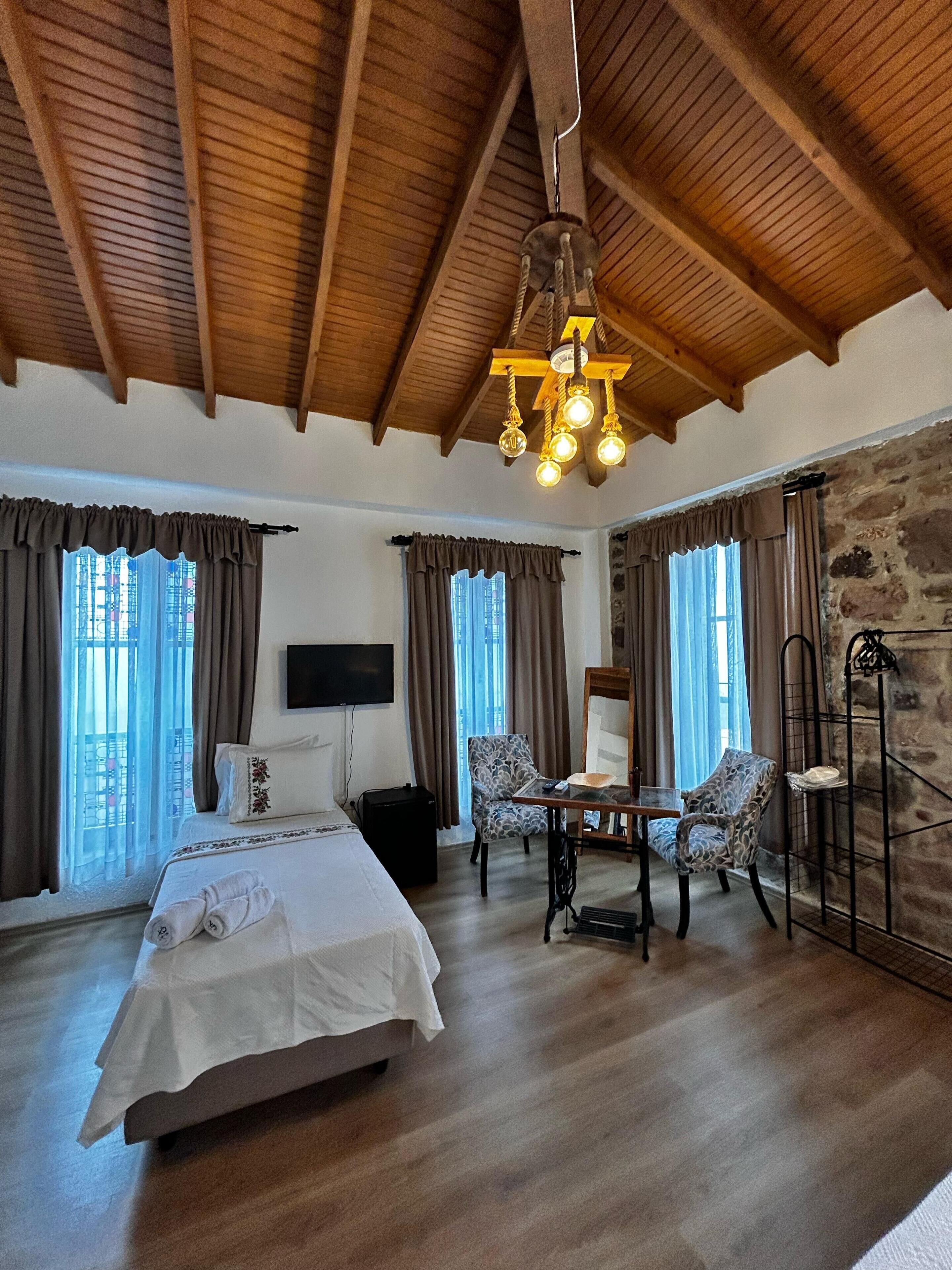 Um quarto espaçoso com uma cama grande, duas cadeiras, uma mesinha, televisão e parede de pedra.