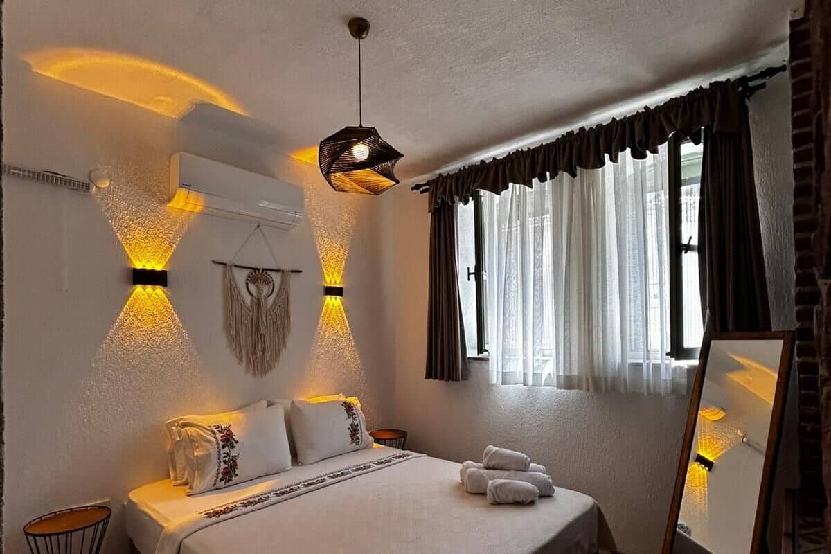 Un dormitorio con cama, lámparas de noche, un espejo y una ventana con cortinas.