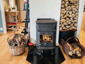 En vedeldad kamin i ett rum med en öppen spis, en hög med ved och två korgar fulla med vedträn.