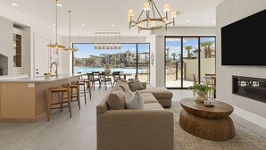 Ein modernes Wohnzimmer mit einer großen Couch, einem Essbereich und Blick auf einen Pool sowie Gebäude.