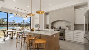Una cocina moderna con una isla grande, taburetes de bar y vistas a una piscina y palmeras.