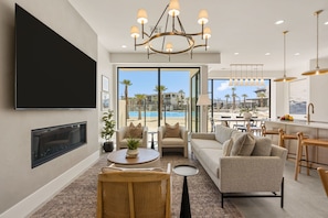 A modern living room with a flat-screen TV, comfortable seating, a chandelier, and a view of a pool. - Barefoot Beach House A + B: Lagoon-Front (St. George)