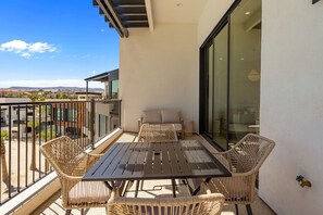 Ein Balkon mit Tisch und Stühlen, einer Couch und einer Glaswand mit Blick auf Gebäude und Hügel.