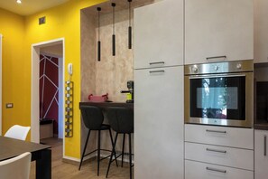 A modern kitchen with a built-in oven, a dining area with a table and chairs, and a yellow accent wall.