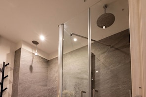 Un baño moderno con cabina de ducha de vidrio, pared de mármol e iluminación integrada.