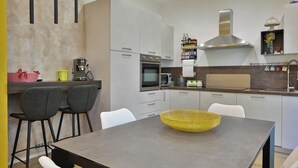 Et moderne køkken med hvide skabe, et rustfrit stål emfang og et spiseområde med et mørkt bord og stole.