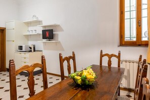 Een eethoek met een houten tafel, stoelen, een schaal fruit, een televisie en keukenapparatuur.
