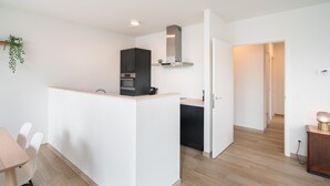 Une cuisine moderne avec un îlot central, un coin repas avec des chaises et un couloir menant à une autre pièce.