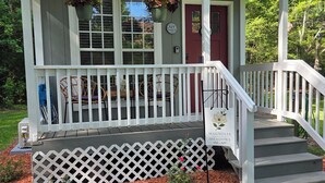A small, single-story building with a porch, a red door, and a staircase leading up to the entrance. - Magnolia Meadows (Hampstead)