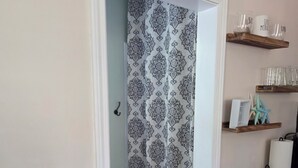 A doorway with patterned curtains, a small shelf with glassware and a starfish decoration, and a black cabinet with a white door. - Magnolia Meadows (Hampstead)