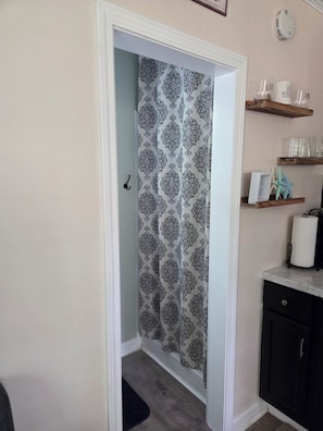 Una porta con tende decorate, un piccolo ripiano con bicchieri e una decorazione a stella marina, e un armadietto nero con una porta bianca.