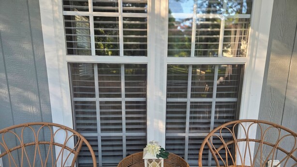 A porch with two wicker chairs and a small table with a lantern. - Magnolia Meadows (Hampstead)