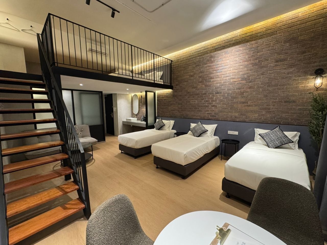 A modern hotel room with a loft-style bed, a staircase, and a brick accent wall.