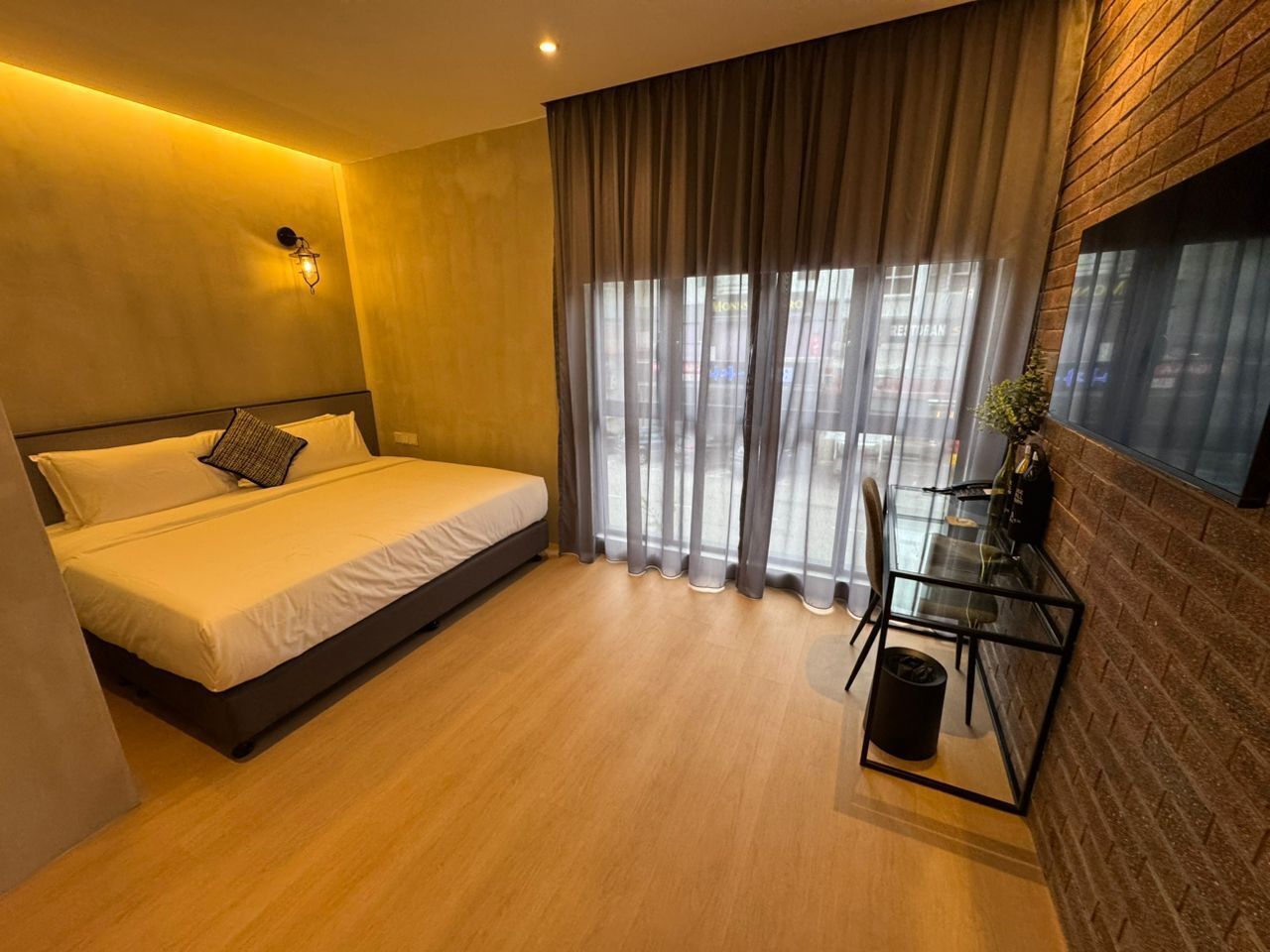 Una habitación de hotel moderna con cama, escritorio y vistas a través de cortinas traslúcidas.