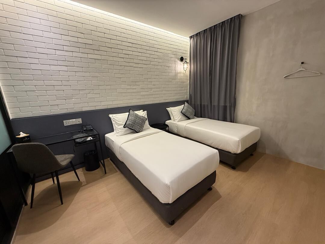 Habitación de hotel con dos camas, un escritorio, una silla, una lámpara colgante y un perchero.