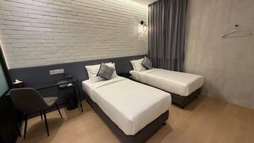Habitación de hotel con dos camas, un escritorio, una silla, una lámpara colgante y un perchero.