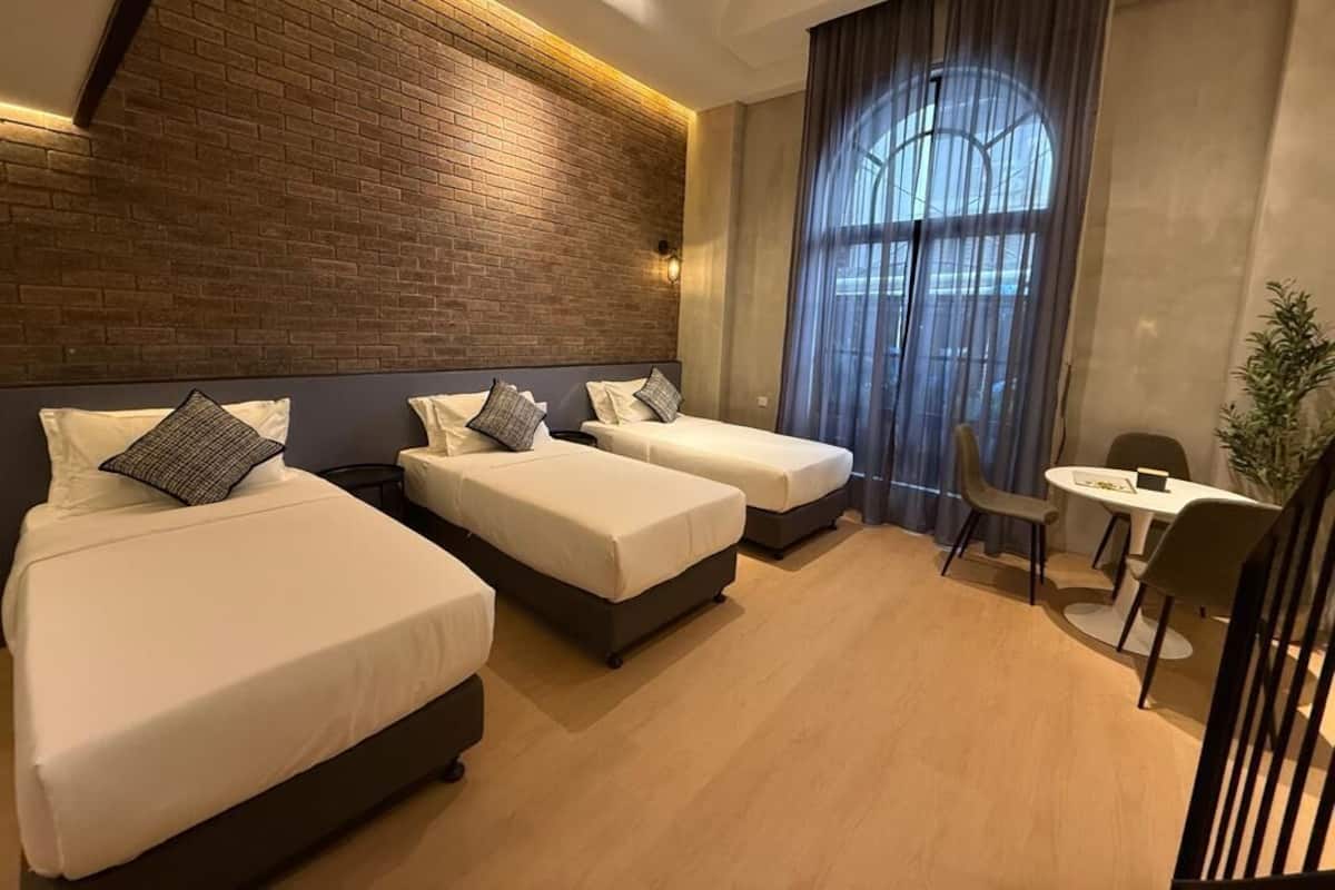 Habitación de hotel con tres camas, zona de comedor y un amplio ventanal con cortinas.