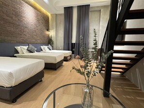 A modern hotel room with two beds, a glass coffee table, a vase with flowers, and a staircase. - Atelier Hotel Permas (Masai)