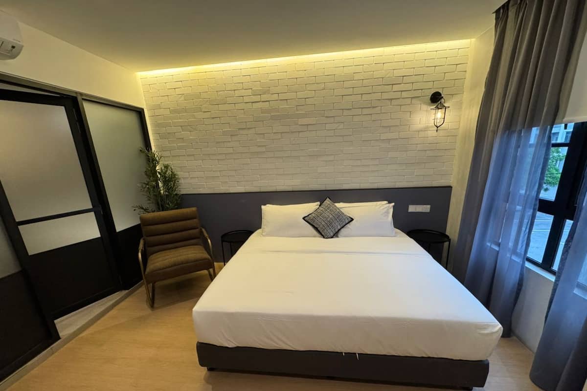 Habitación de hotel moderna con una cama grande, una silla, una lámpara de pared y una ventana con cortinas.