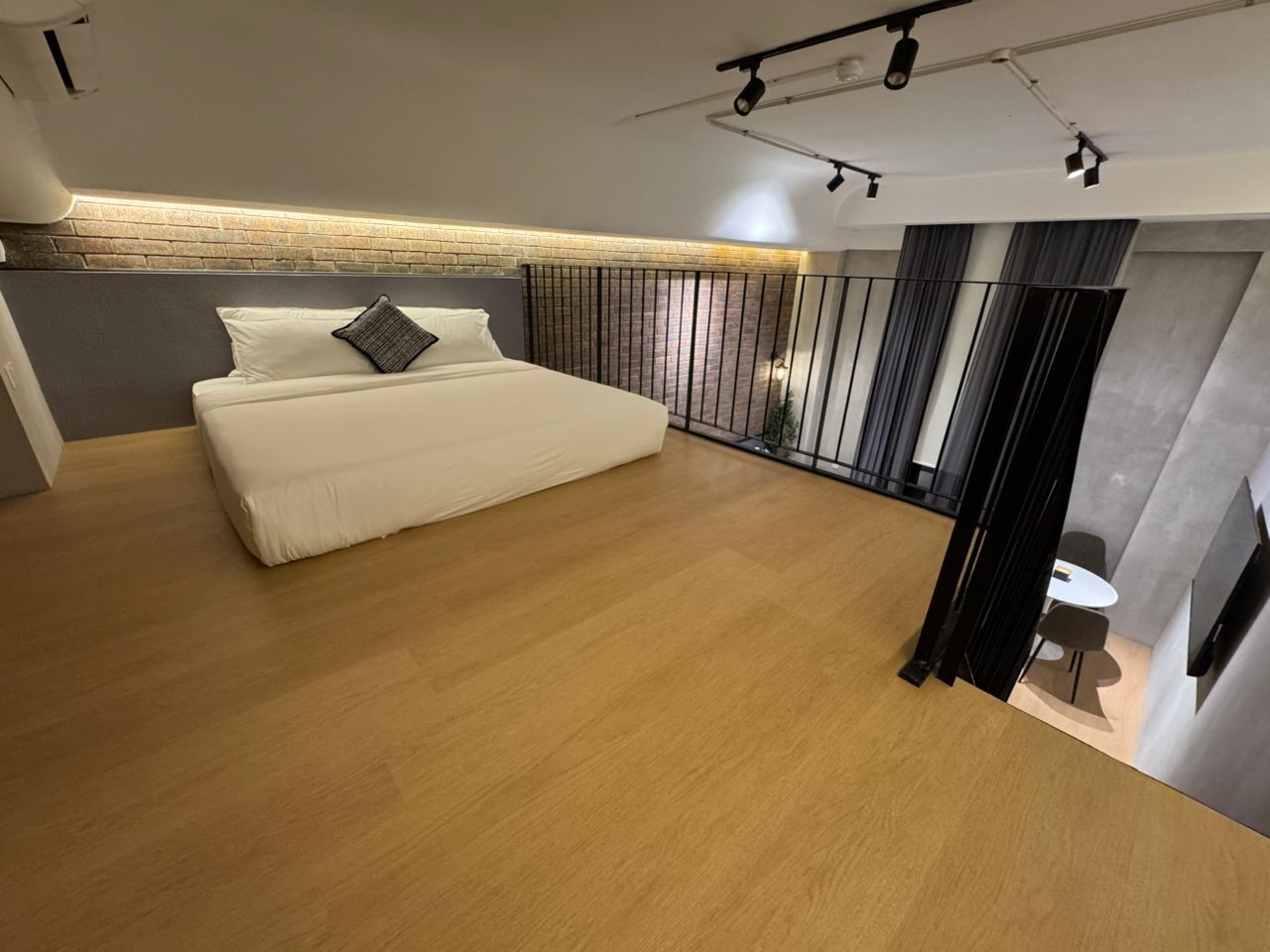 Un dormitorio con una cama grande, piso de madera, pared de ladrillo decorativa y balcón con cortinas.