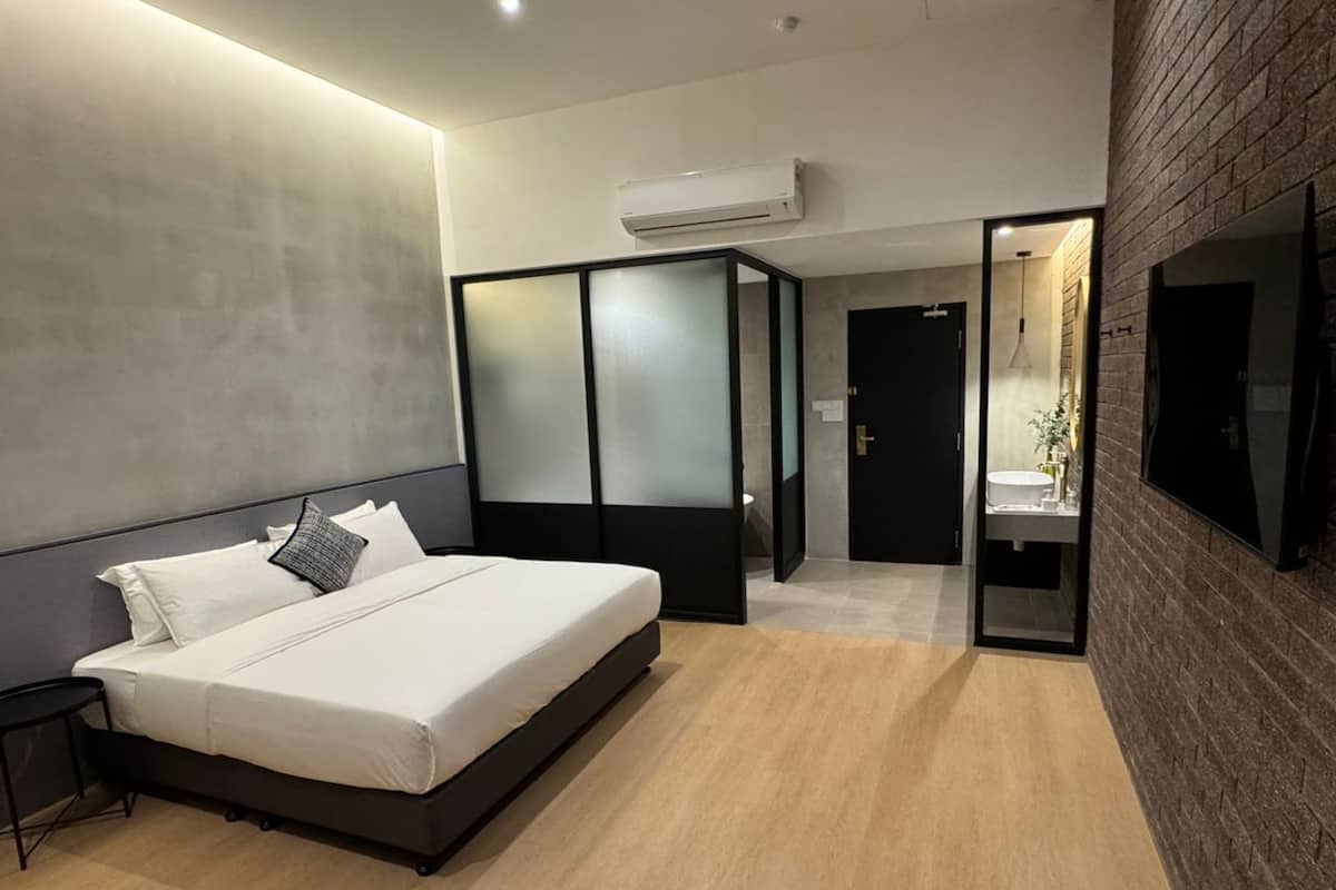 Un dormitorio moderno con cama, mesita de noche, televisión instalada en la pared y baño visible a través de una puerta abierta.