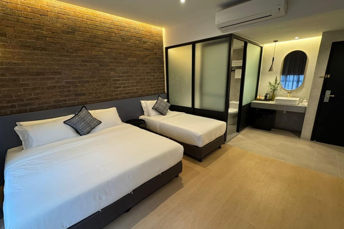Una habitación de hotel moderna con dos camas, un baño con un espejo grande y suelo de madera.