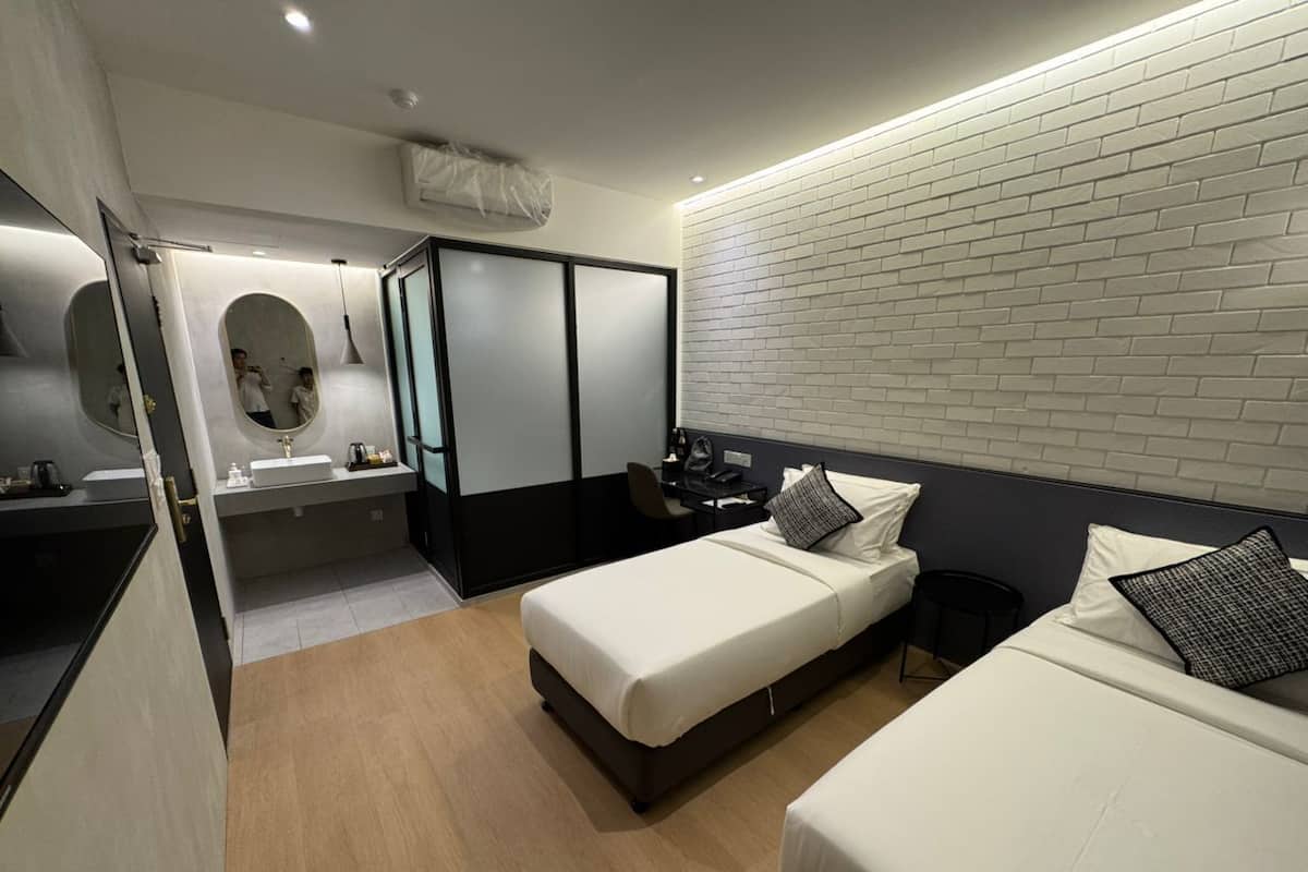 Una habitación de hotel moderna con dos camas, un escritorio, una silla, un espejo y un baño con lavamanos e inodoro.