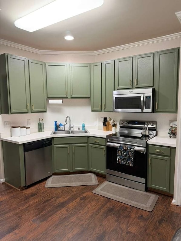 A kitchen with green cabinets, a stainless steel dishwasher, a microwave, and a stove.