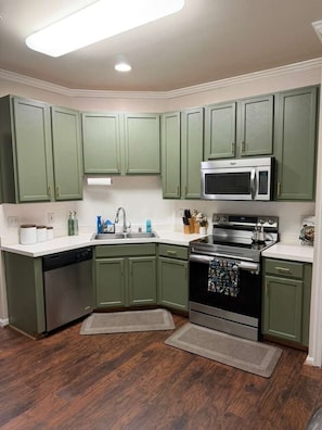 A kitchen with green cabinets, a stainless steel dishwasher, a microwave, and a stove.