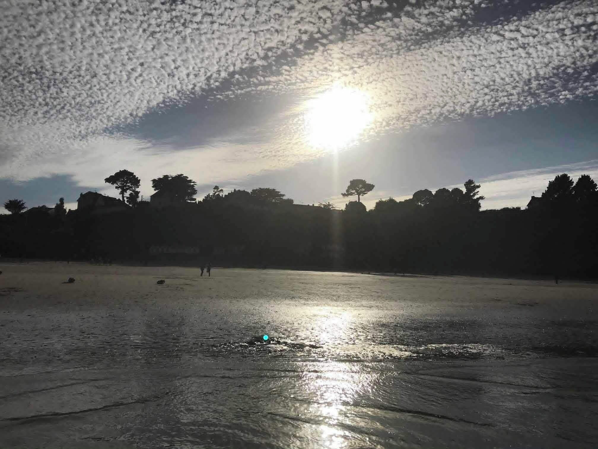 Una playa con el sol bajo en el horizonte, proyectando un reflejo sobre la arena mojada.