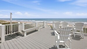 A wooden deck with white railings, white Adirondack chairs, and a view of the ocean.