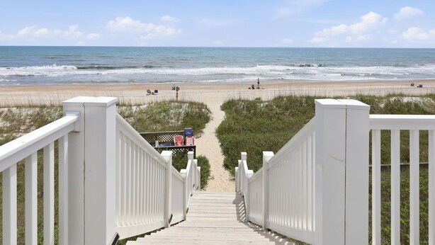A wooden staircase leading to a beach with a fence and a lifeguard tower.