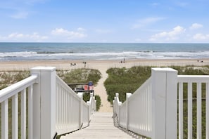 A wooden staircase leading to a beach with a fence and a lifeguard tower.