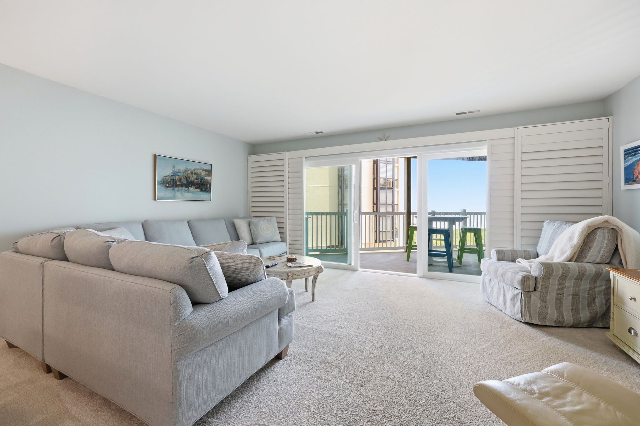 A living room with a sofa, armchair, and a small table. There is a sliding glass door leading to an outdoor area.