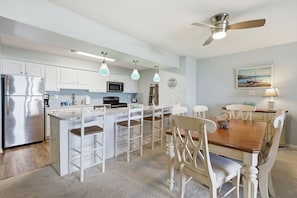 A modern kitchen with white cabinets, a stainless steel refrigerator, a microwave, and a dining area with a wooden table and white chairs.