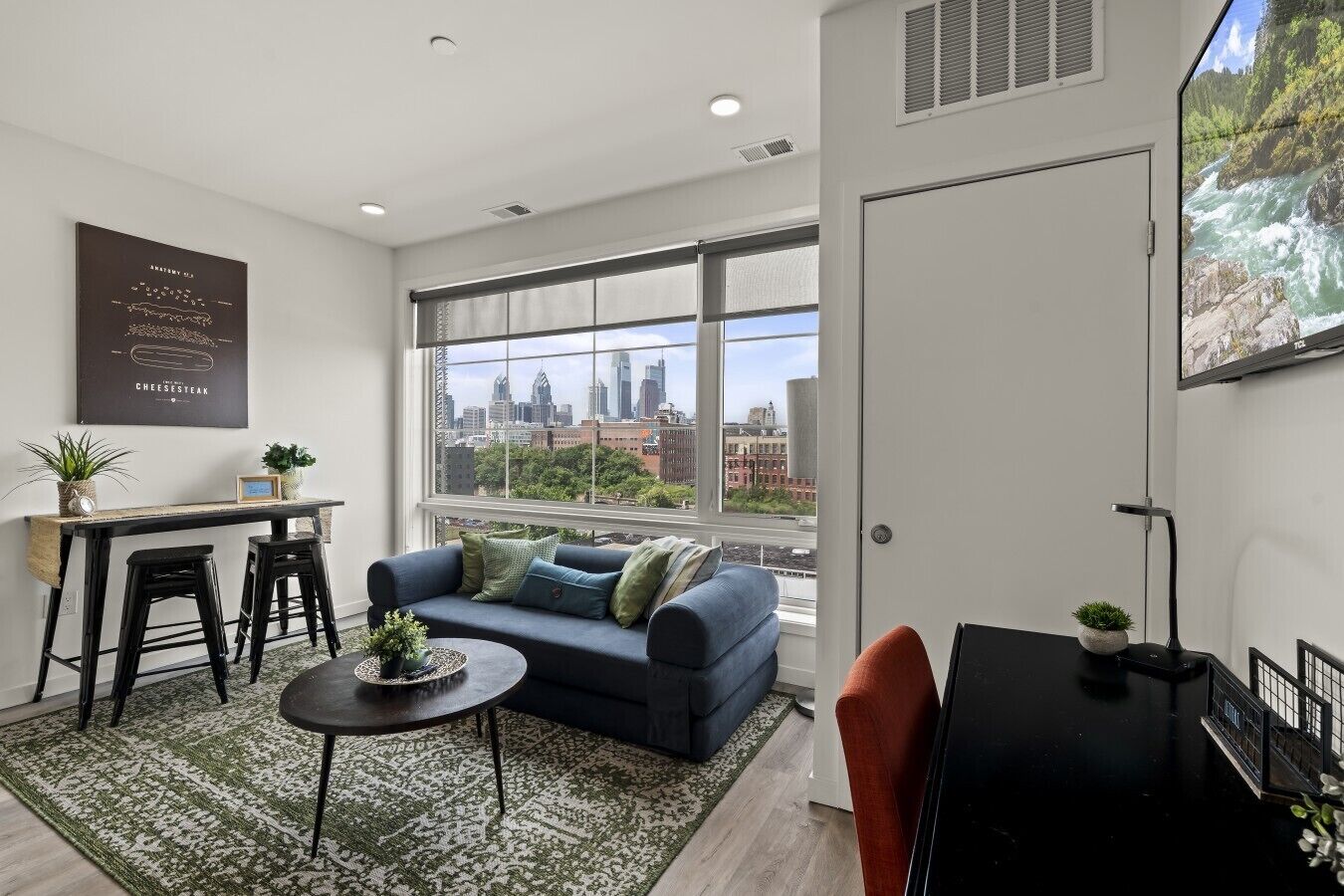 Ein modernes Wohnzimmer mit einer Couch, einem Couchtisch und Blick auf die Stadt durch große Fenster.