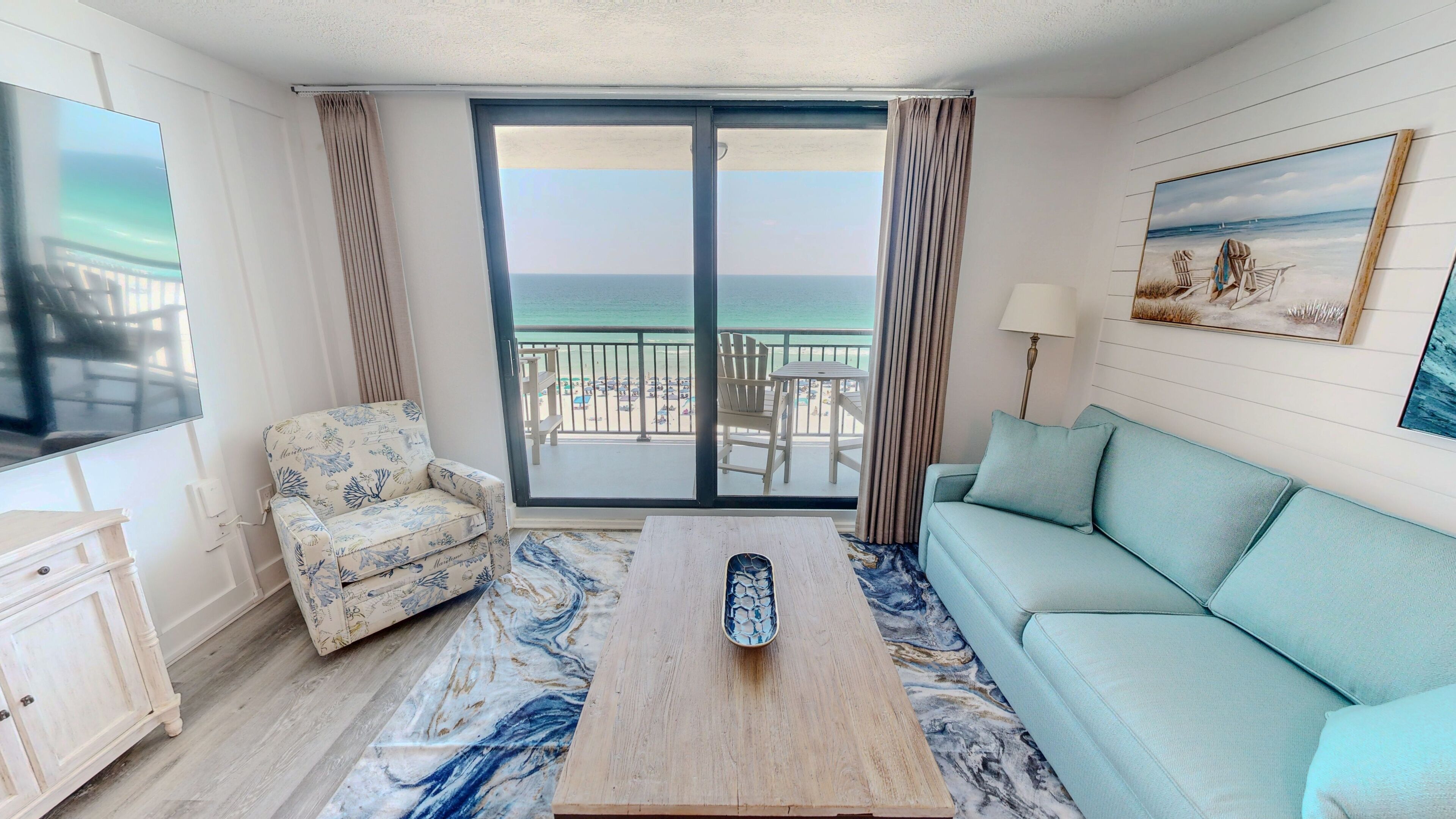Une pièce comprenant un canapé, un fauteuil, une table basse, un téléviseur et un balcon avec vue sur la mer.
