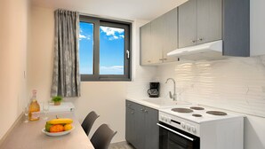 Une cuisine compacte avec une fenêtre, une machine à café, une cuisinière et une table à manger agrémentée de fruits et de verres.